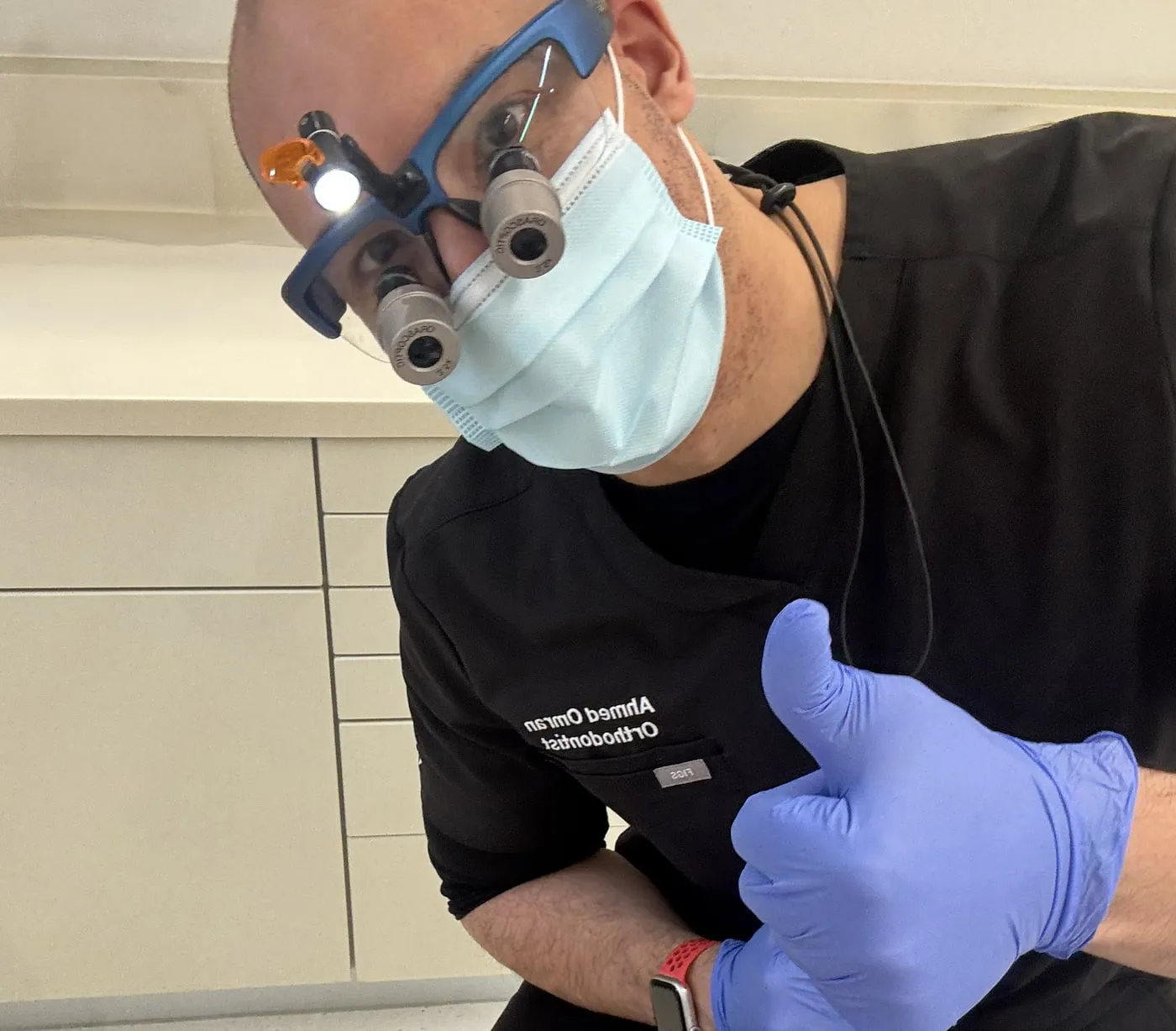 Dr Ahmed Omran in clinic, wearing magnifying loupes and giving a thumbs up